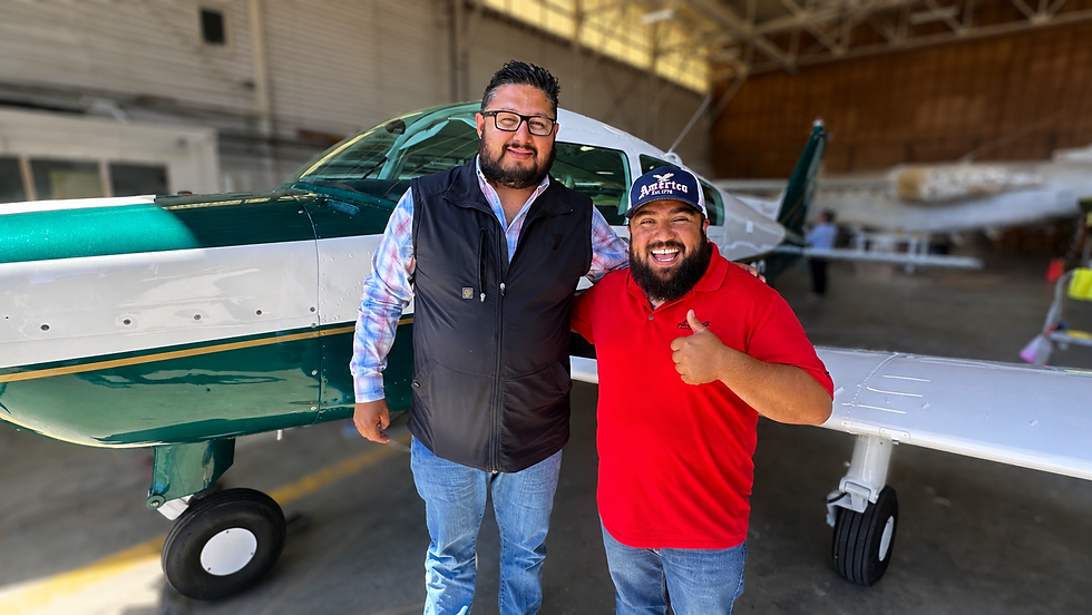 Two people smiling and standing in front of a small airplane inside a hangar, landscape photo, aviation theme, bright colors.