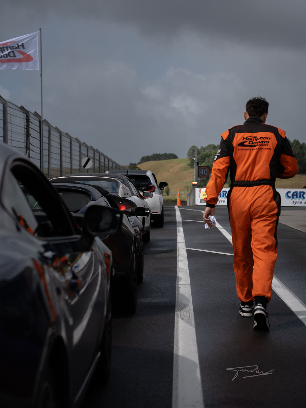 Racer in orange suit walks on wet track past cars