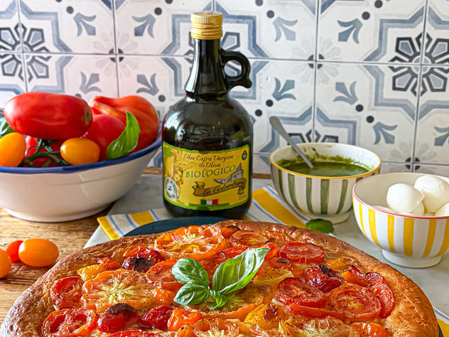 Focaccia al pomodoro soffice e dorata, preparata con concentrato di pomodoro nell’impasto, guarnita con pomodori freschi a fette, pesto leggero di basilico e olio extravergine d’oliva.