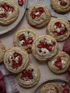Knusprige Cookies mit weißer Schokolade und Mandeln, dekoriert mit kleinen Klecksen Erdbeermarmelade und gefriergetrockneten Erdbeeren, leicht goldbraun gebacken, außen knusprig und innen weich.