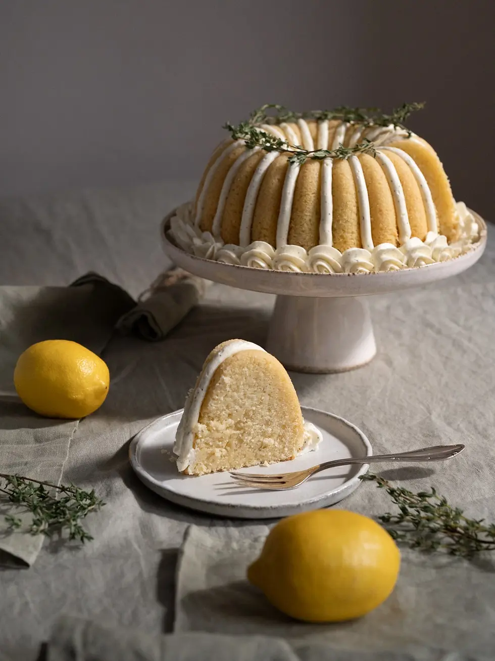 Zitronen-Thymian-Gugelhupf mit dekorativer Pudding-Buttercreme, Zitronen und Thymian auf einer Tortenplatte
