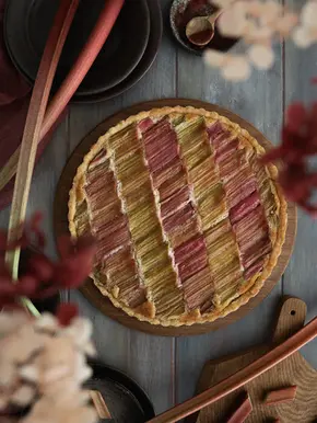 Vegane Rhabarber Frangipane Tarte in einer flachen Tarteform mit goldbraunem, mürbem Boden. Auf der saftigen Mandel-Frangipane liegen rosa-grüne Rhabarberstücke dekorativ angeordnet. Die frühlingshafte Tarte wirkt außen knusprig und innen weich und saftig.