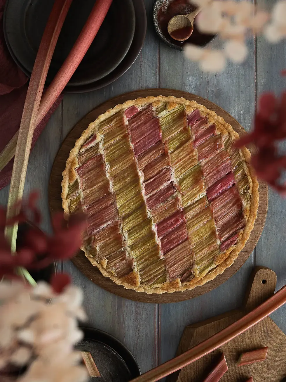 Vegane Rhabarber Frangipane Tarte in einer flachen Tarteform mit goldbraunem, mürbem Boden. Auf der saftigen Mandel-Frangipane liegen rosa-grüne Rhabarberstücke dekorativ angeordnet. Die frühlingshafte Tarte wirkt außen knusprig und innen weich und saftig.