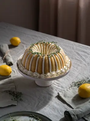 Zitronen-Thymian-Gugelhupf mit dekorativer Pudding-Buttercreme, Zitronen und Thymian auf einer Tortenplatte