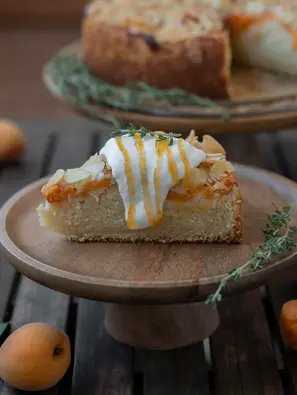 Ein Stück Aprikosen Mandel Kuchen, dekoriert mit einem Klecks Sahne und einem Streifenmuster aus Aprikosenmarmelade.
