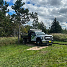 Urban Roots branded truck parked on lawn with trees at the edge, long trench in ground visible behind truck and running to right side of screen.
