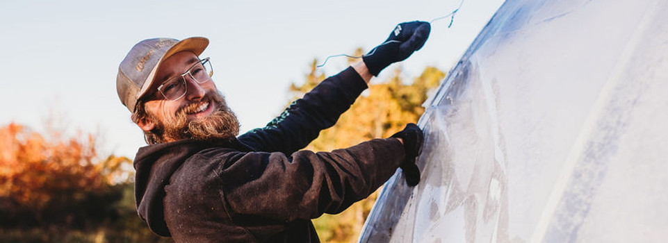 Worker smiling and posing as they apply plastic to a greenhouse
