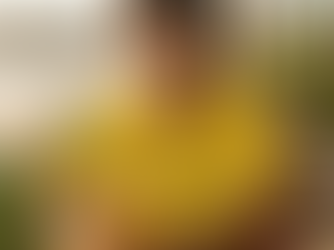 Modelo masculino sorridente em um quiosque de praia, vestindo a camiseta amarela 'maracujá' da 4Life Creative com estampa preta. Ele segura um suco de maracujá, conectando a moda premium ao conceito de Calmaria Tropical da Coleção Brasilidade.