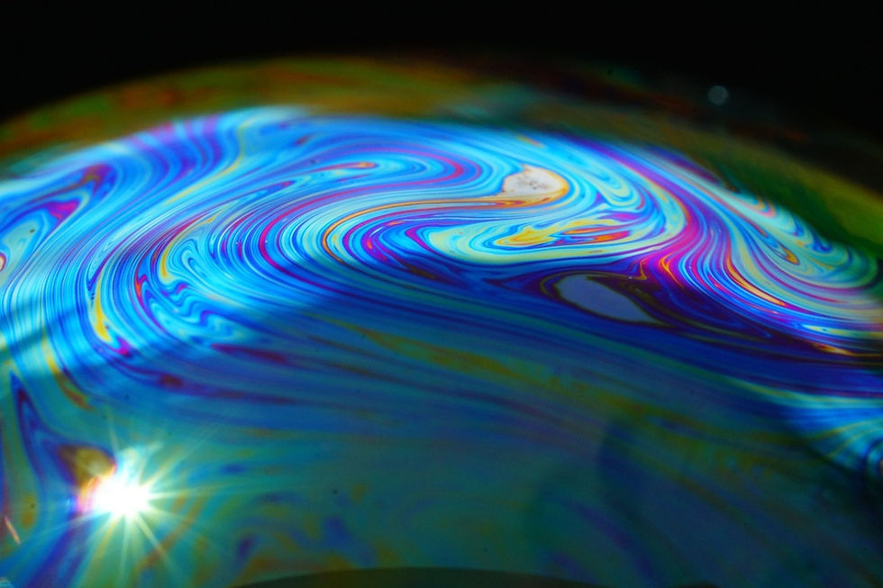Swirling vibrant colors on a soap bubble's surface reflect light, creating an abstract, kaleidoscopic pattern against a dark background.