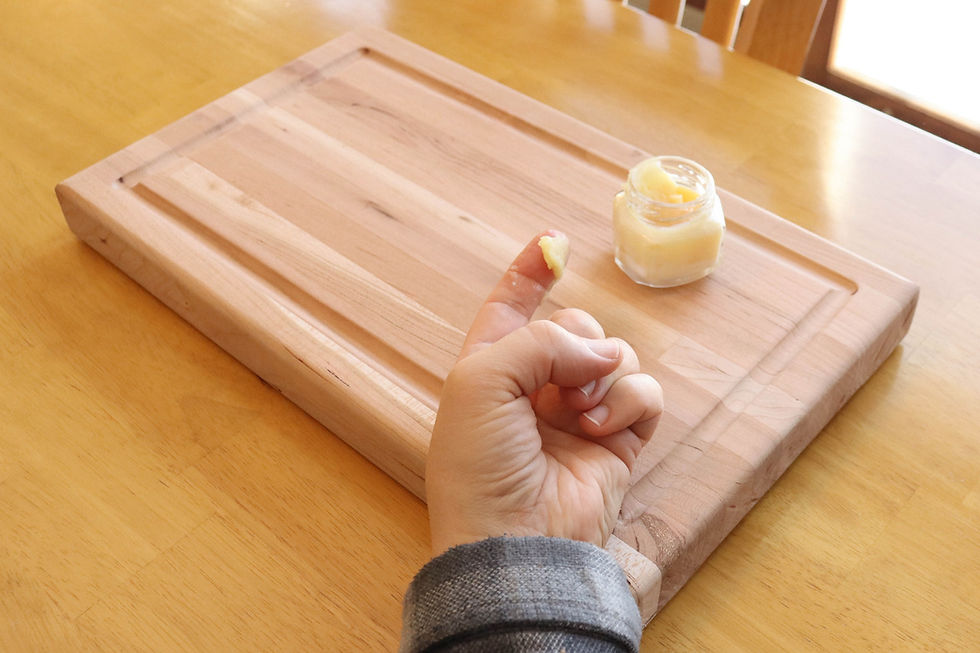 A hand with wood finish on fingers, next to a small jar on a wooden cutting board. Warm lighting and a cozy kitchen ambiance.