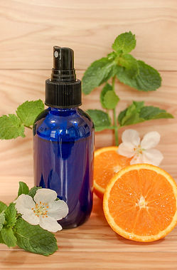A blue spritzer bottle surrounded by white flowers and slices of citrus fruit