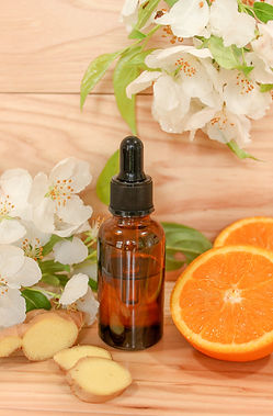 An amber glass dropper bottle filled with an essential oil body oil and surrounded by white flowers and slices of organic ginger root