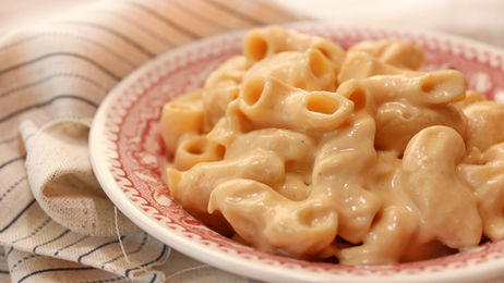 Creamy vegan macaroni and cheese on a red-patterned plate set on a striped cloth. The dish looks warm and inviting, evoking comfort.
