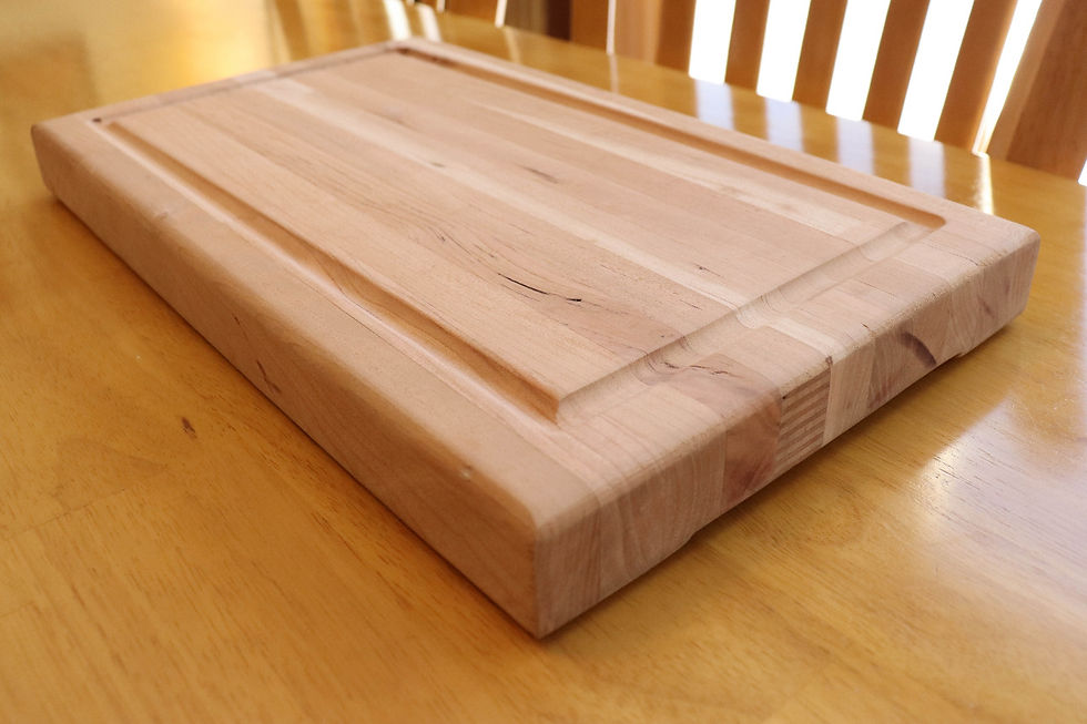 Wooden cutting board on a light brown table. The board has a groove along the edge and displays natural wood patterns.