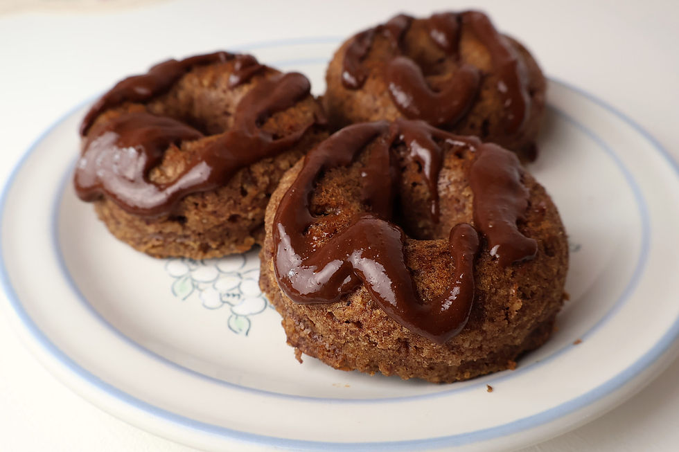 Three apple cinnamon donuts drizzled with chocolate glaze on a white plate with blue rim, close-up on a light background.