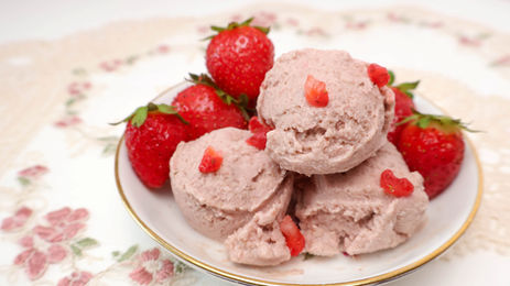 Vegan strawberry ice cream scoops topped with diced strawberries and whole berries on a floral plate, fresh and sweet