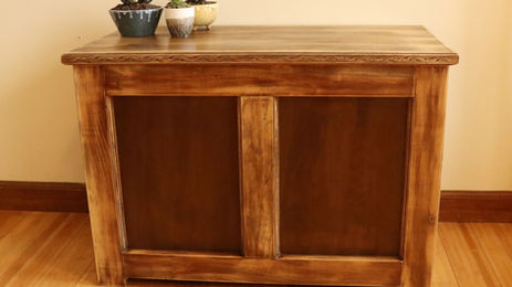 Wooden cabinet with intricate carvings, topped by three small potted succulents in colorful pots. Set against a beige wall on a wooden floor. It's fully finished with this diy all-natural wood stain
