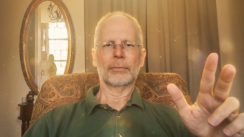 Bald man with glasses in a green shirt sits on a patterned chair, gesturing with fingers. A mirror and window are in the background.
