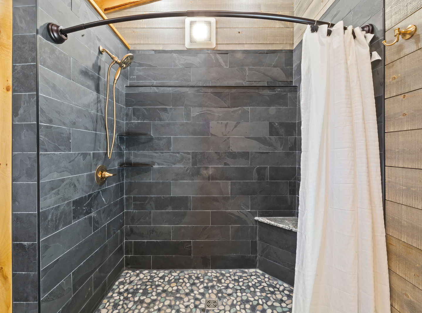 Small, modern bathroom with dark tiles and white curtain.