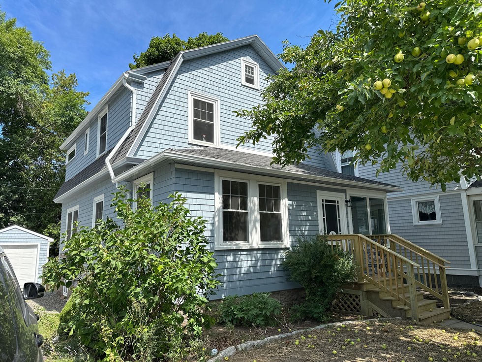 Blue house with white trim and surrounding greenery.