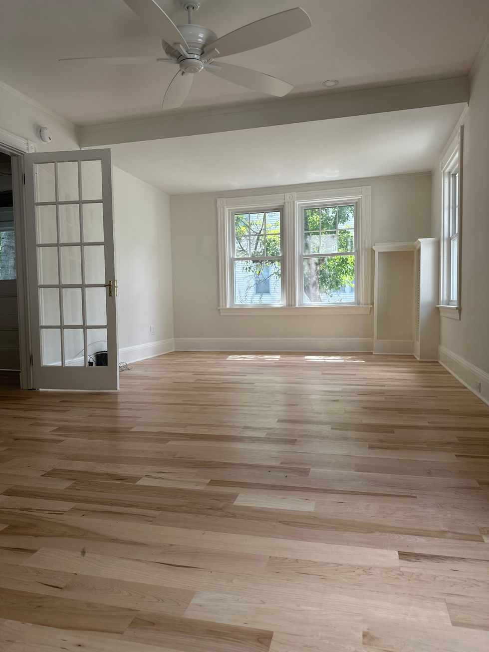 Bright, empty room with wooden floor and large windows.