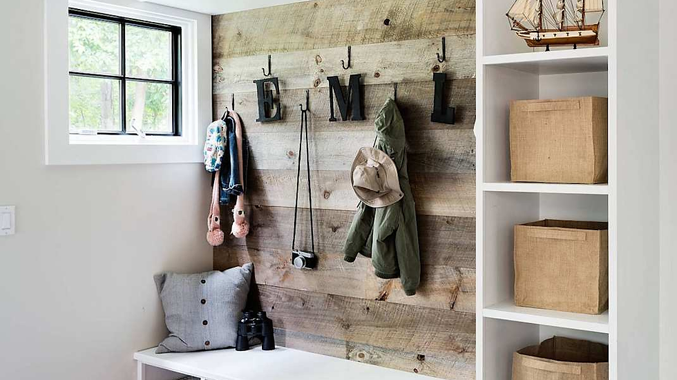 Mudroom with wooden wall hooks displaying clothes. Shelf holds a model ship. Storage bins house shoes and sports gear. Calm, organized space.