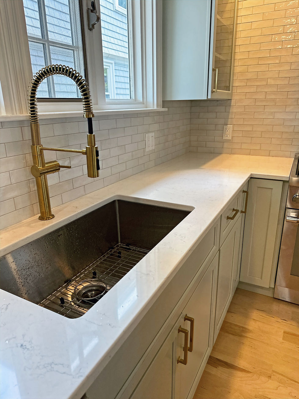 Modern kitchen with a large stainless sink, gold spring faucet, white tile backsplash, and window-lit counter.