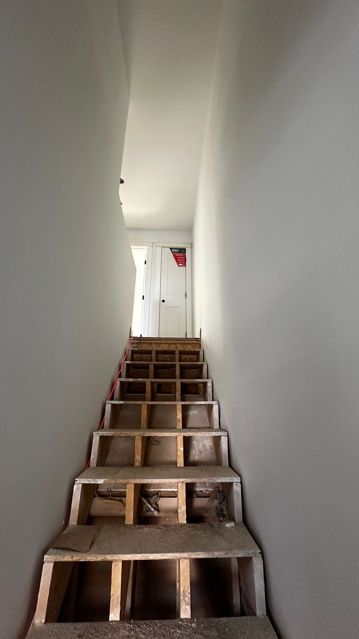Narrow staircase with wooden steps and white walls.