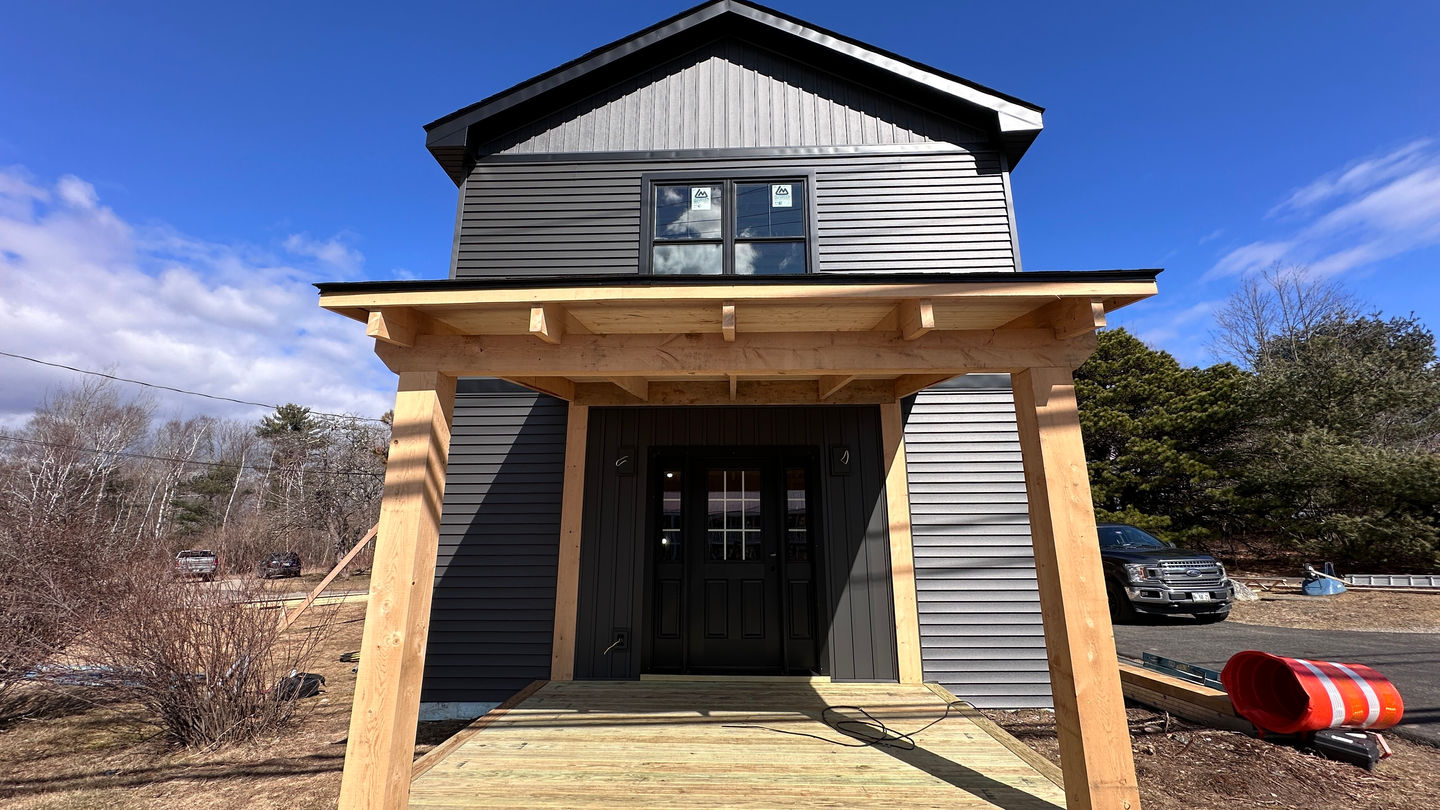 Small modern house with wooden porch and black door.