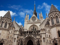 Gothic Royal Courts of Justice building in London with spires and arched entrance under a bright blue sky.