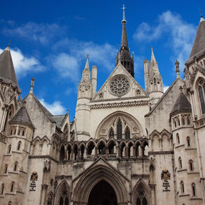 Gothic Royal Courts of Justice building in London with spires and arched entrance under a bright blue sky.