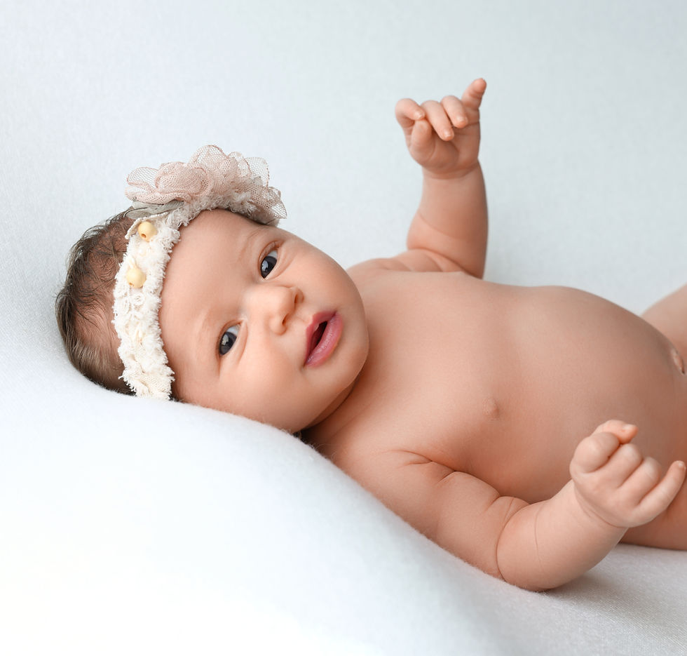 Awake newborn baby girl lying on a soft white background, gazing curiously during a professional studio photoshoot in San Diego