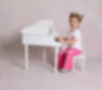 Toddler playing a white mini grand piano on soft pink background, dressed in pink sprinkle pants and flower crown, San Diego photography studio