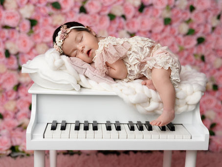 Baby girl sleeping on white grand piano with pink floral backdrop, captured by Irina Dream Photography in San Diego