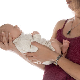Mother’s hands holding newborn baby boy dressed in white outfit, studio portrait in San Diego.
