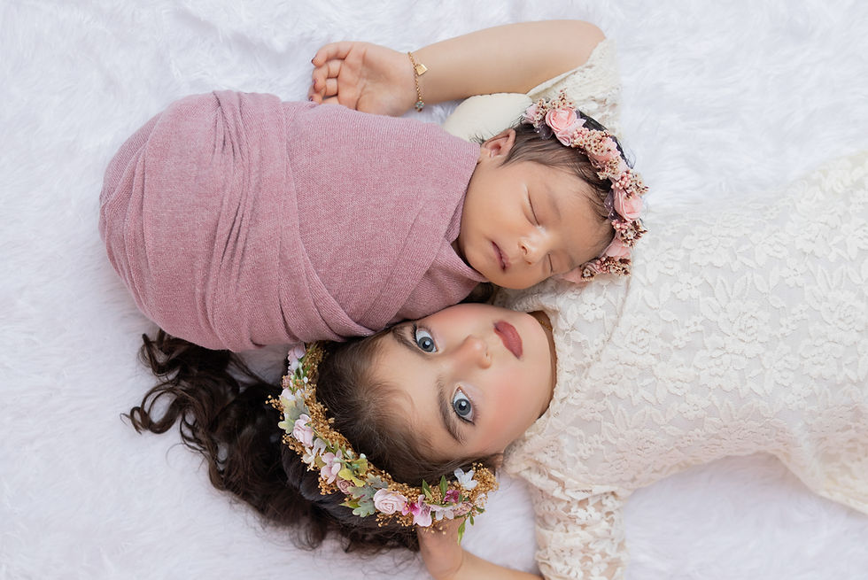 Newborn girl and her sister laying on white backgroundduring photo session in San Diego newborn studio