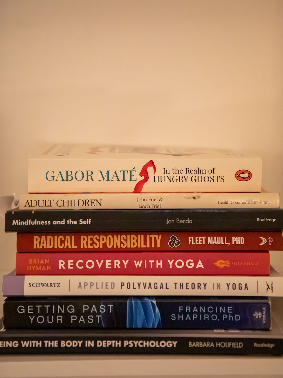 Stack of psychology and yoga books on a shelf, with titles like Gabor Maté, Mindfulness and the Self, and Recovery with Yoga, Polyvagal Theory