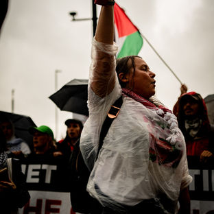 Female at Palestine march holding a tambourine with one arm raised in the air