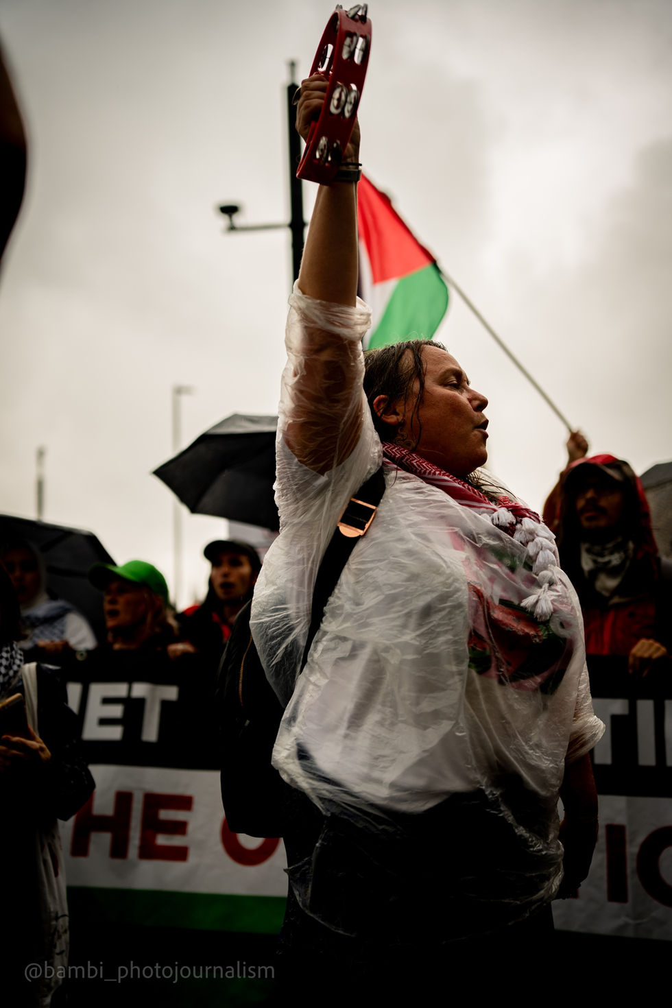 Female at Palestine march holding a tambourine with one arm raised in the air