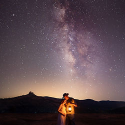 A pregnant mother and her husband embrace as they hold a lantern under the stars