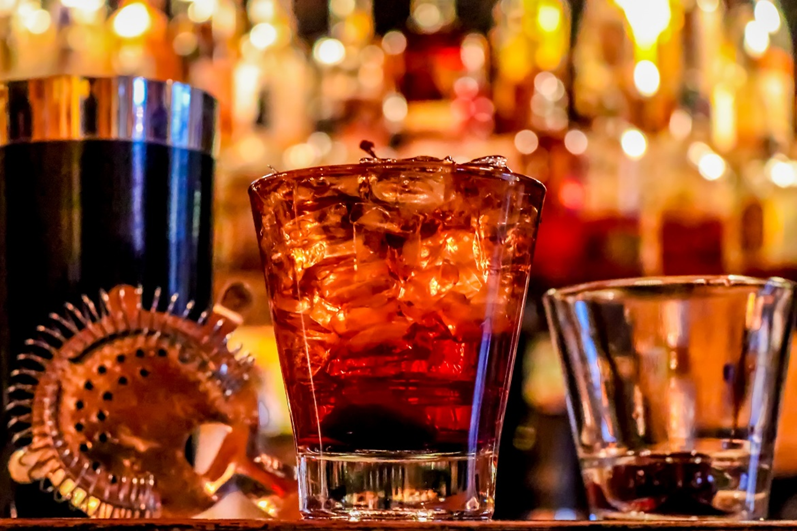 A Hawthorne cocktail strainer with two glasses, one filled with whiskey and ice cubes.