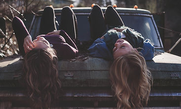 Two girls with long hair laying with their knees up and hair hanging down, having a conversation
