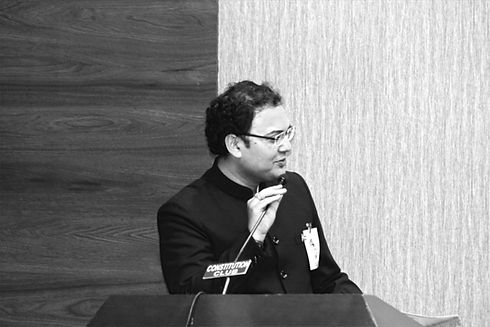Man Arpit Chaturvedi wearing black jacket sherwani speaking into a mic