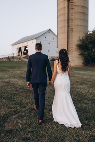 bride and groom walking towards their white barn wedding venue