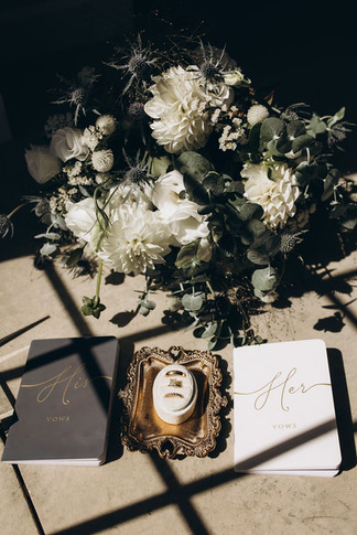 his and her vow books, wedding rings and bridal bouquet cast in shadow