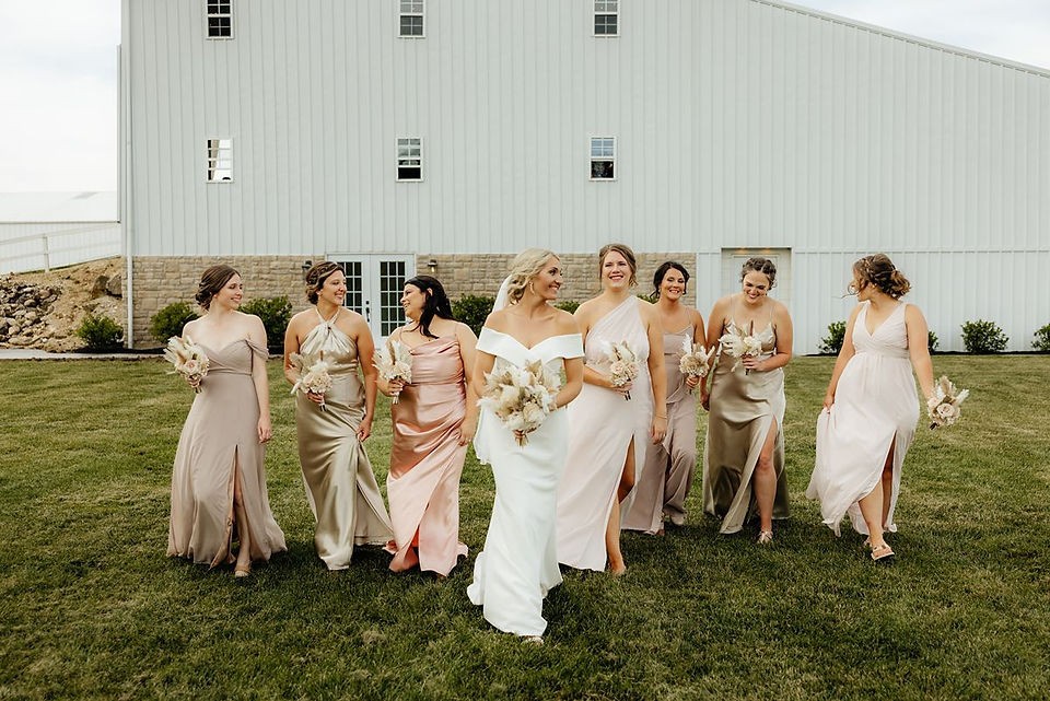 bride walking in front of white barn with boho bridesmaids