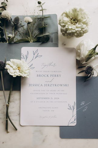 blue and white wedding invitation surrounded by white wildflowers
