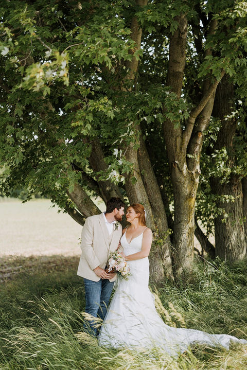 bride and groom caressing under a tree in long grass