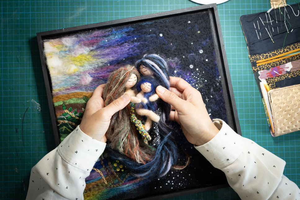 Hands arranging textile dolls on a colorful, star-patterned felt artwork.