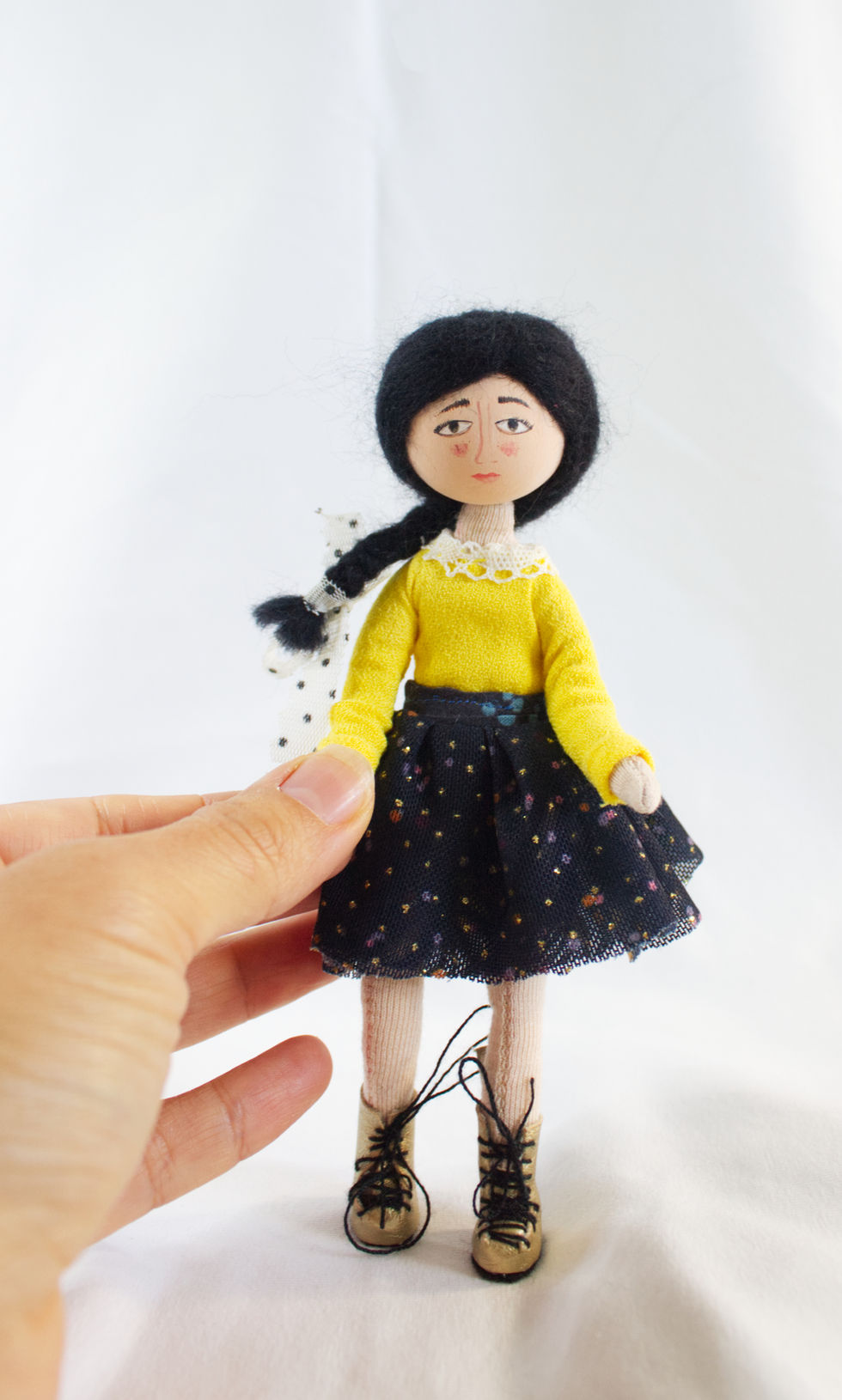 Handmade felt and wood puppet of a girl with black braids, wearing a yellow blouse and dark skirt, created with textile and embroidery details.